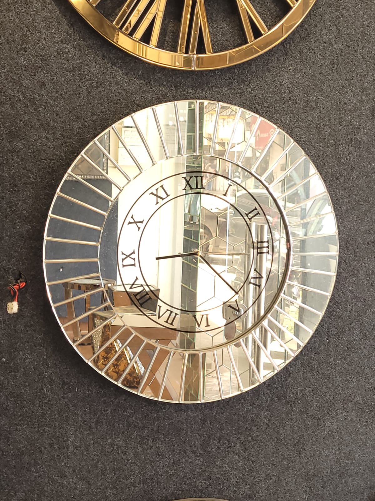 Silver sunburst clock — Radial mirrored segments surround a Roman-numeral clock face.